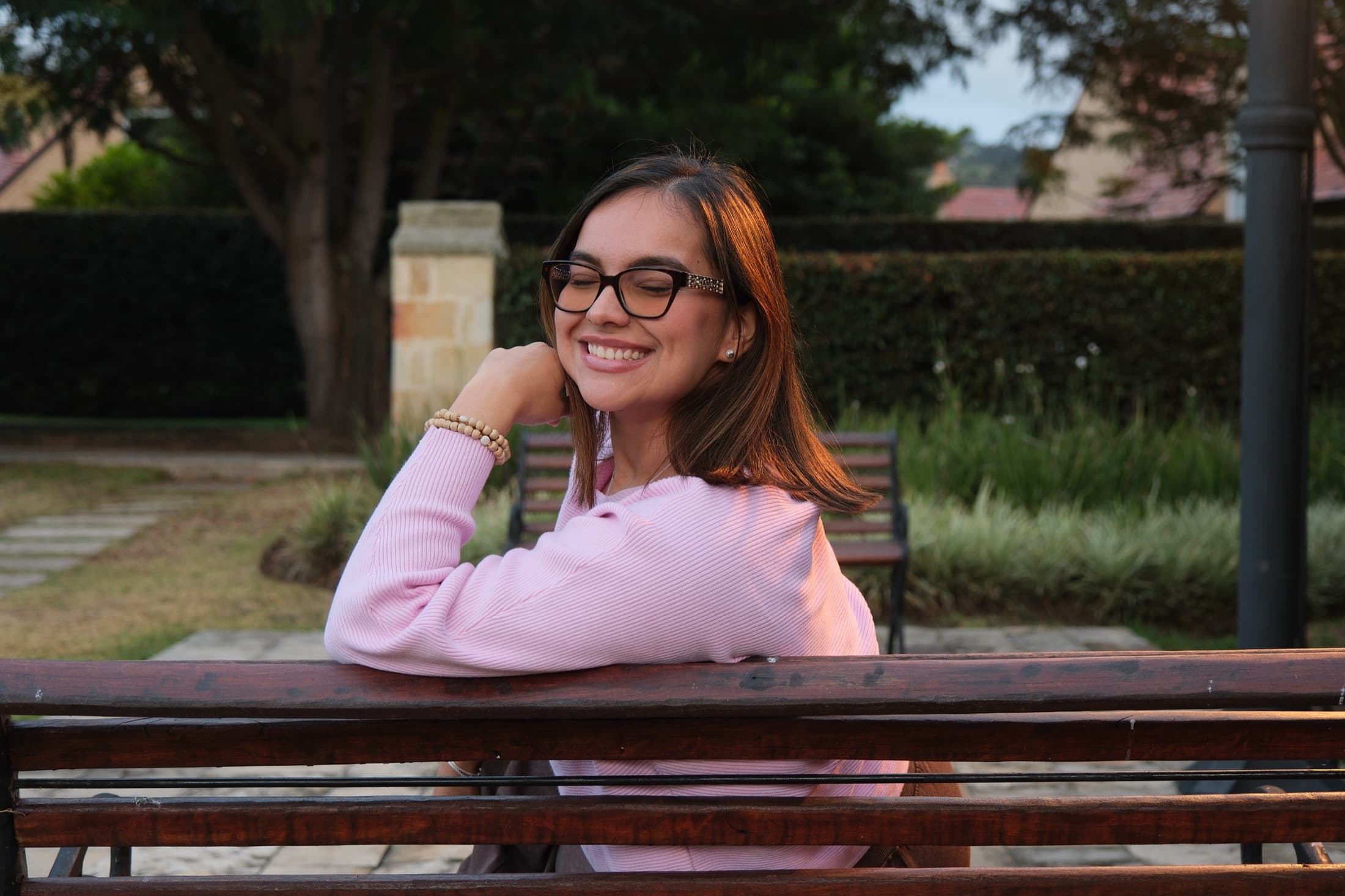 Angélica Cabrera sonriendo, apoyada en una banca de madera al atardecer.